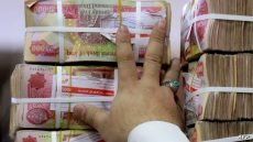 An employee arranges stacks of Iraqi dinars at currency exchange shop in Baghdad on February 14, 2023. Iraq nudged up the value of its local currency against the dollar in an effort to stabilise the dinar after tougher foreign transfer regulations sent its value fluctuating. The government adopted a new official exchange rate, fixing it at 1,300 dinars to the US dollar instead of 1,470, the prime minister's office said. (Photo by Murtaja LATEEF / AFP)